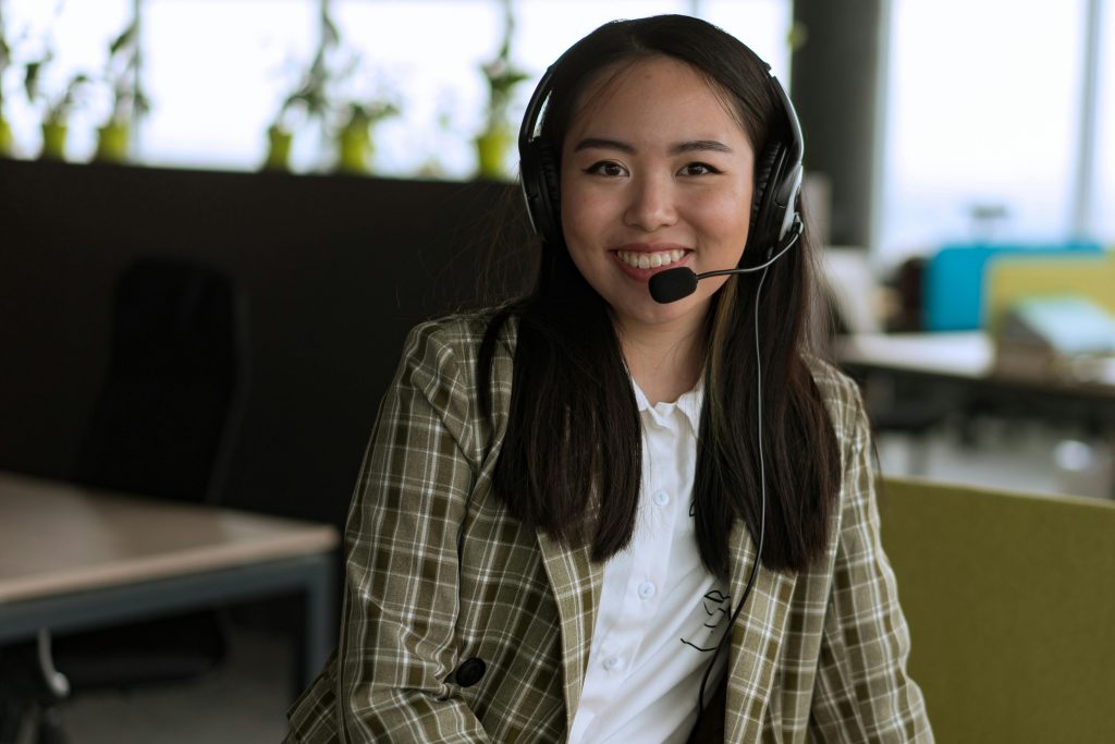 Smiling woman in office wearing a headset, providing customer support in a modern workspace.